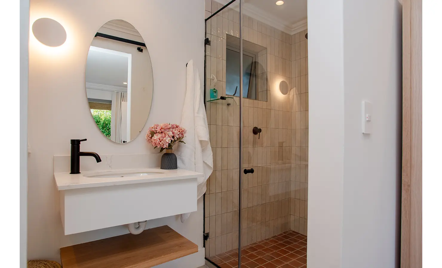 Perfect Hideaways: A modern en-suite bathroom features a walk-in shower with neutral tiles, an oval mirror, and soft lighting that highlights the minimal, elegant design. River Run, Plettenberg Bay.