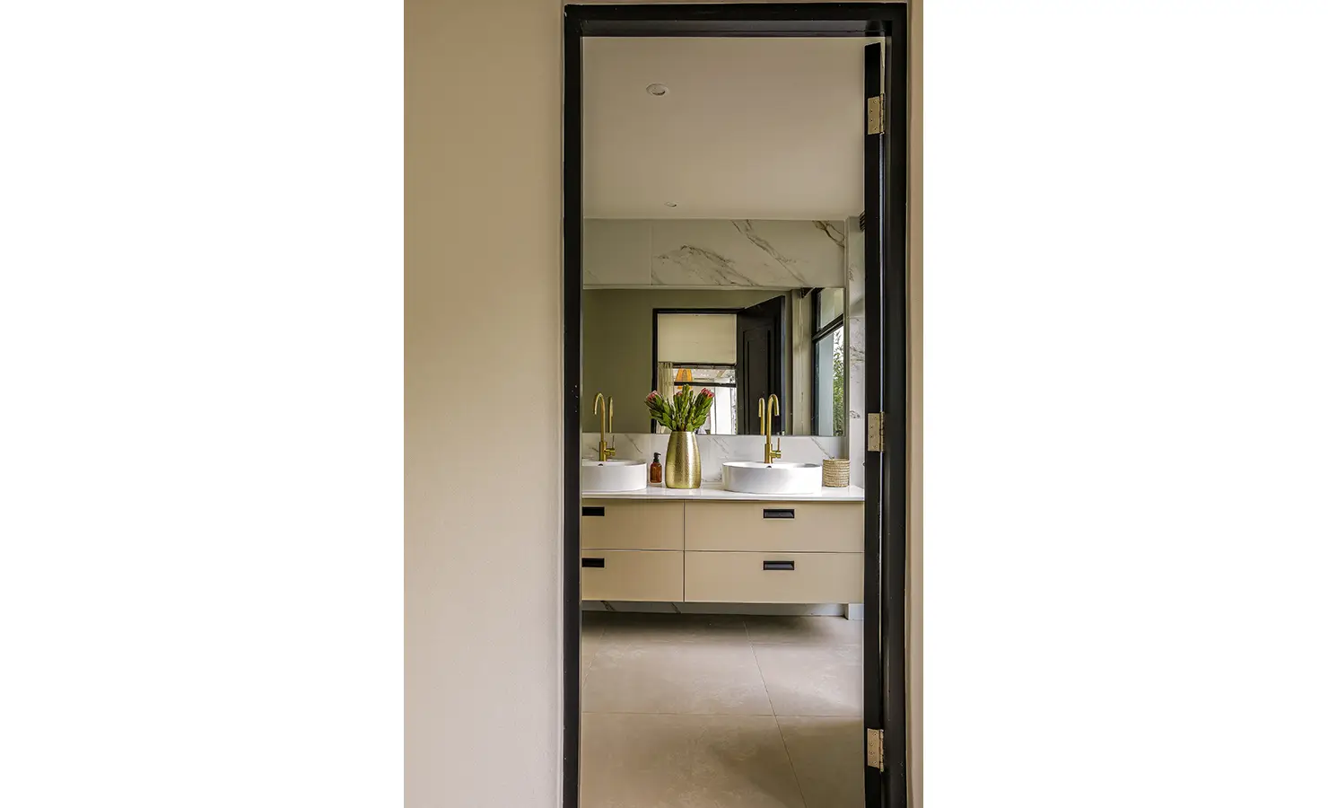 Perfect Hideaways: A modern bathroom with dual basins, golden taps, and a large mirror reflecting natural light through black-trimmed windows. Bel Ombre Hills, Constantia.