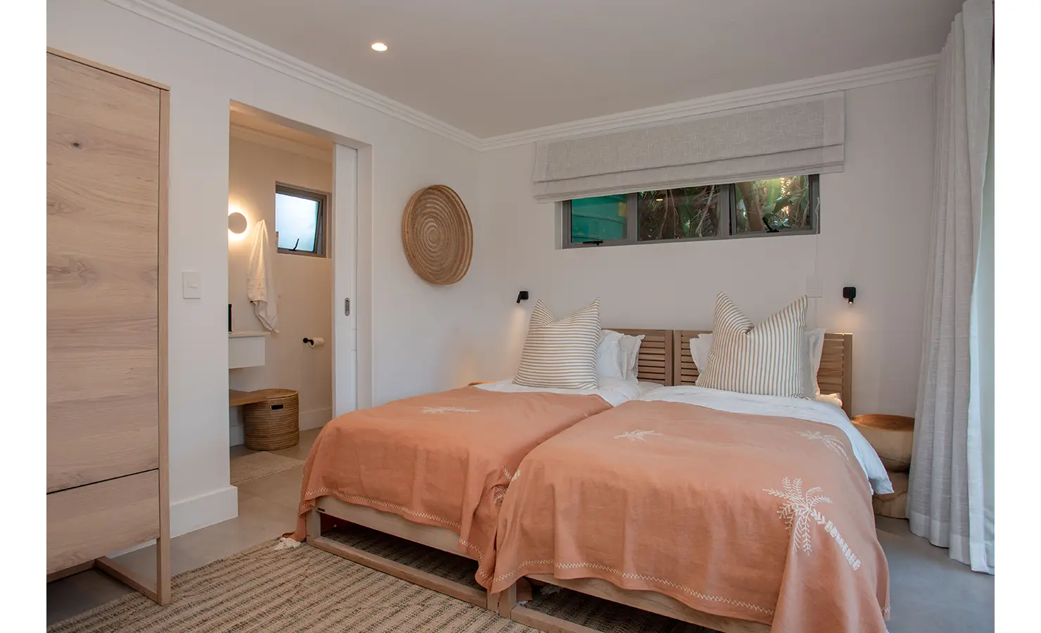Perfect Hideaways: A twin bedroom styled in earthy tones and subtle stripes exudes laid-back charm, with sliding doors leading to a private garden patio. River Run, Plettenberg Bay.