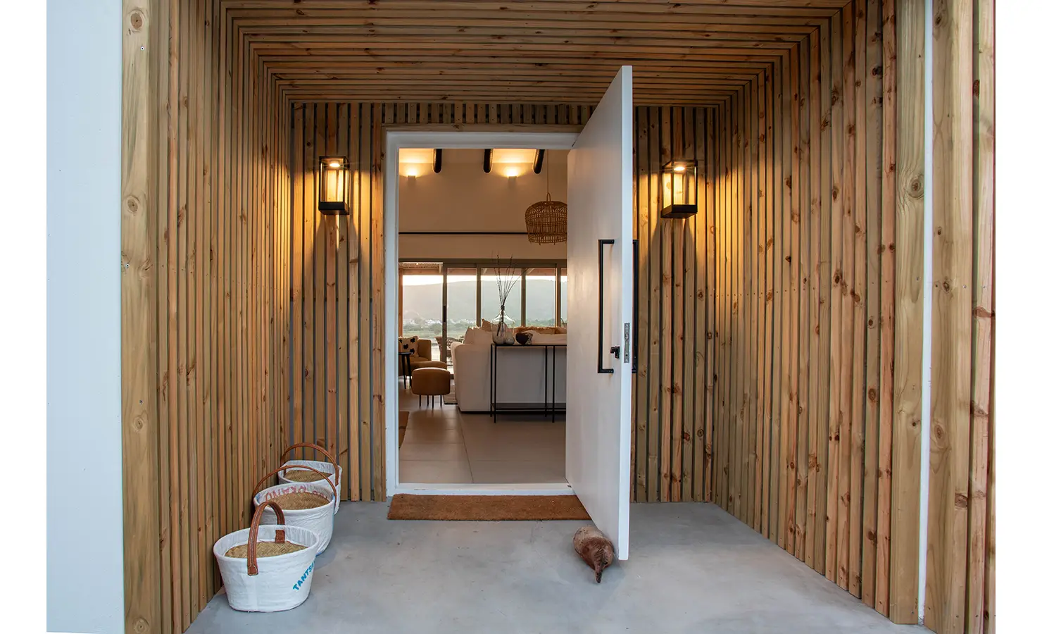 Perfect Hideaways: A striking entranceway framed in vertical wooden slats opens to reveal a view through the home’s stylish interiors toward the river beyond. River Run, Plettenberg Bay.