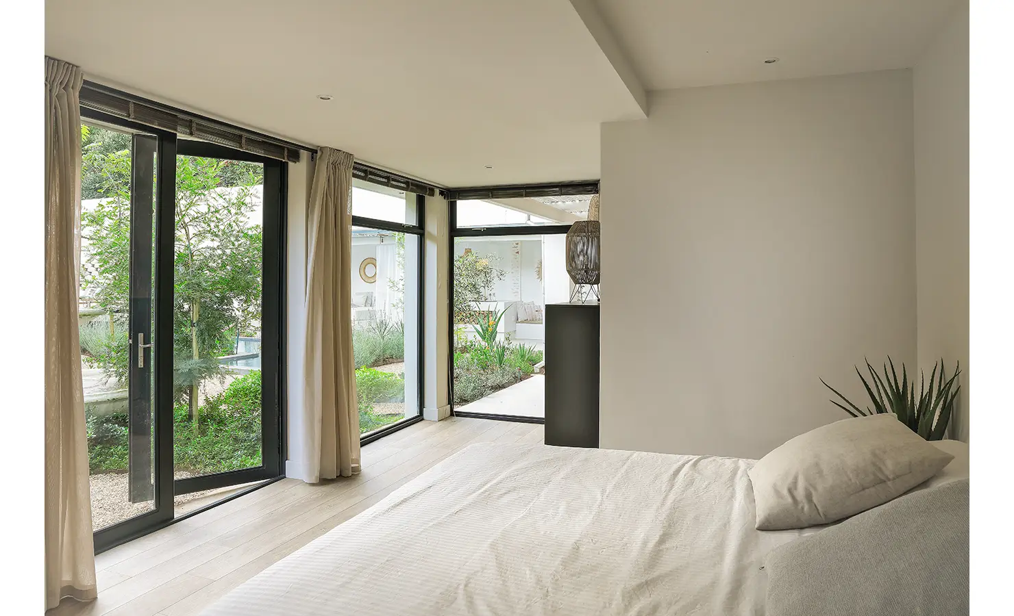 Perfect Hideaways: A serene bedroom view through glass doors and windows onto landscaped gardens, with minimal furnishings and soft natural light. Bel Ombre Hills, Constantia.
