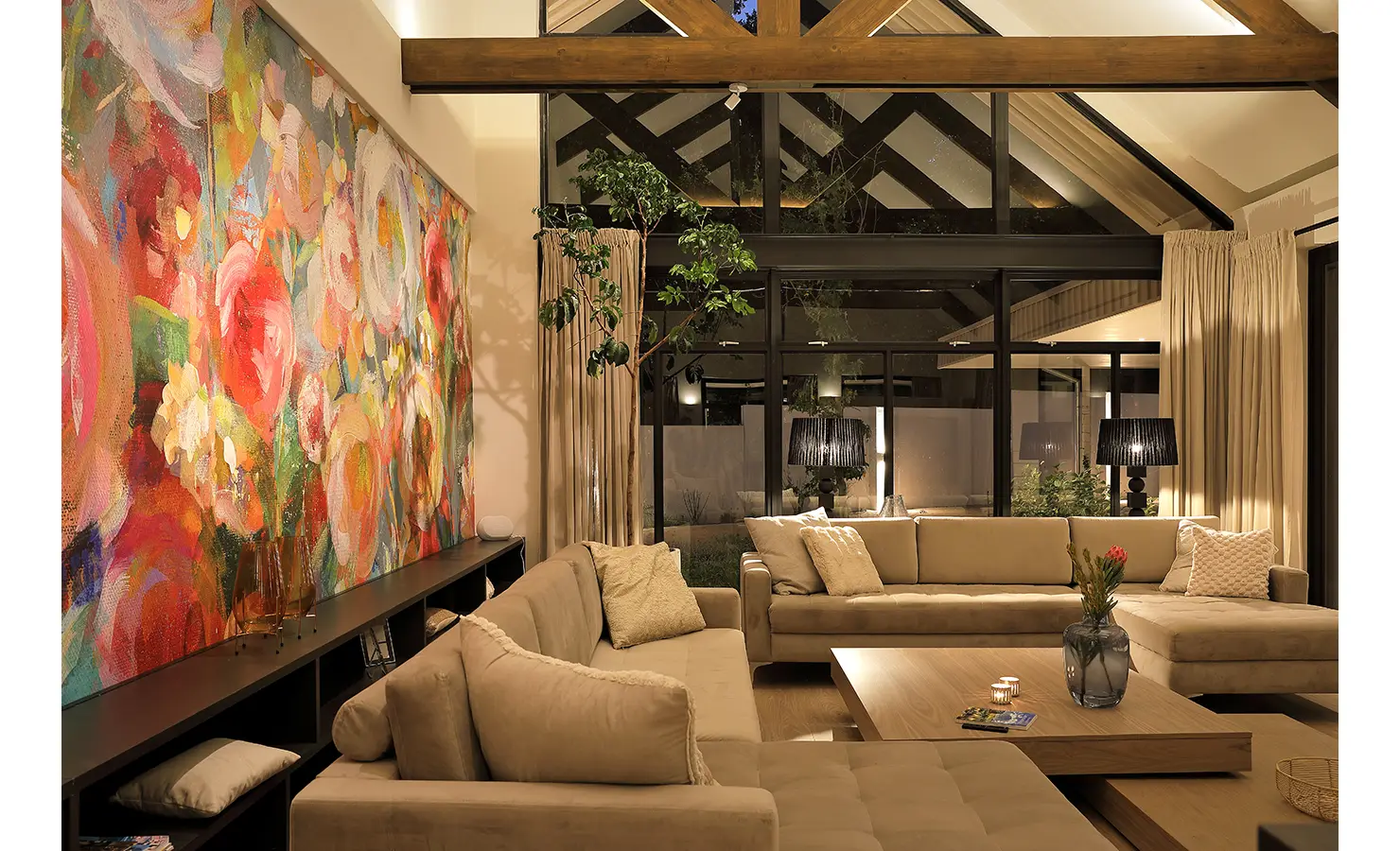 Perfect Hideaways: A dramatic living room with vaulted ceilings, neutral-toned sofas, and a large, vibrant floral mural creating a bold contrast. Bel Ombre Hills, Constantia.