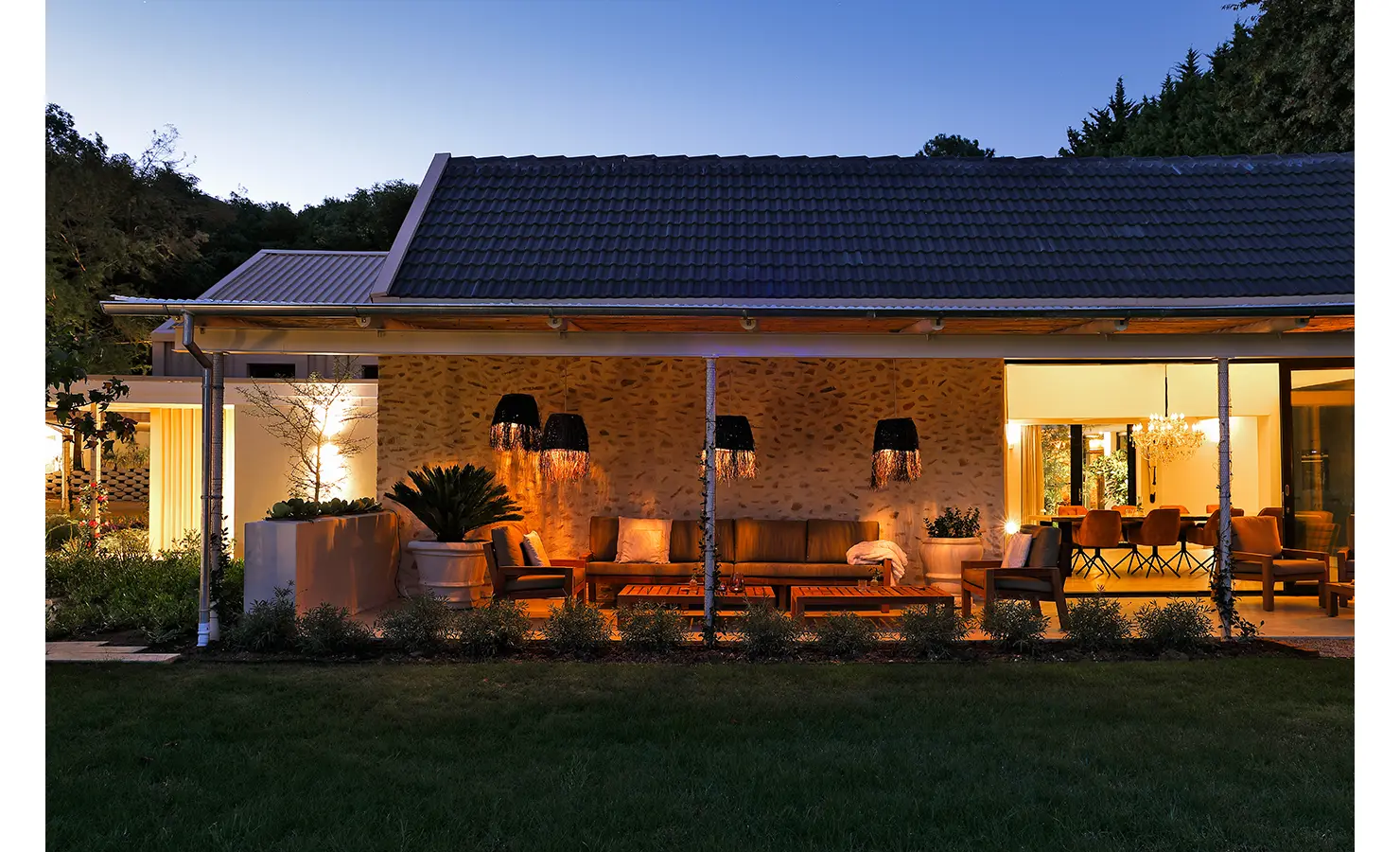 Perfect Hideaways: An inviting evening scene on the veranda with moody lighting, wicker pendant lamps, and glimpses into the elegant dining room beyond. Bel Ombre Hills, Constantia
