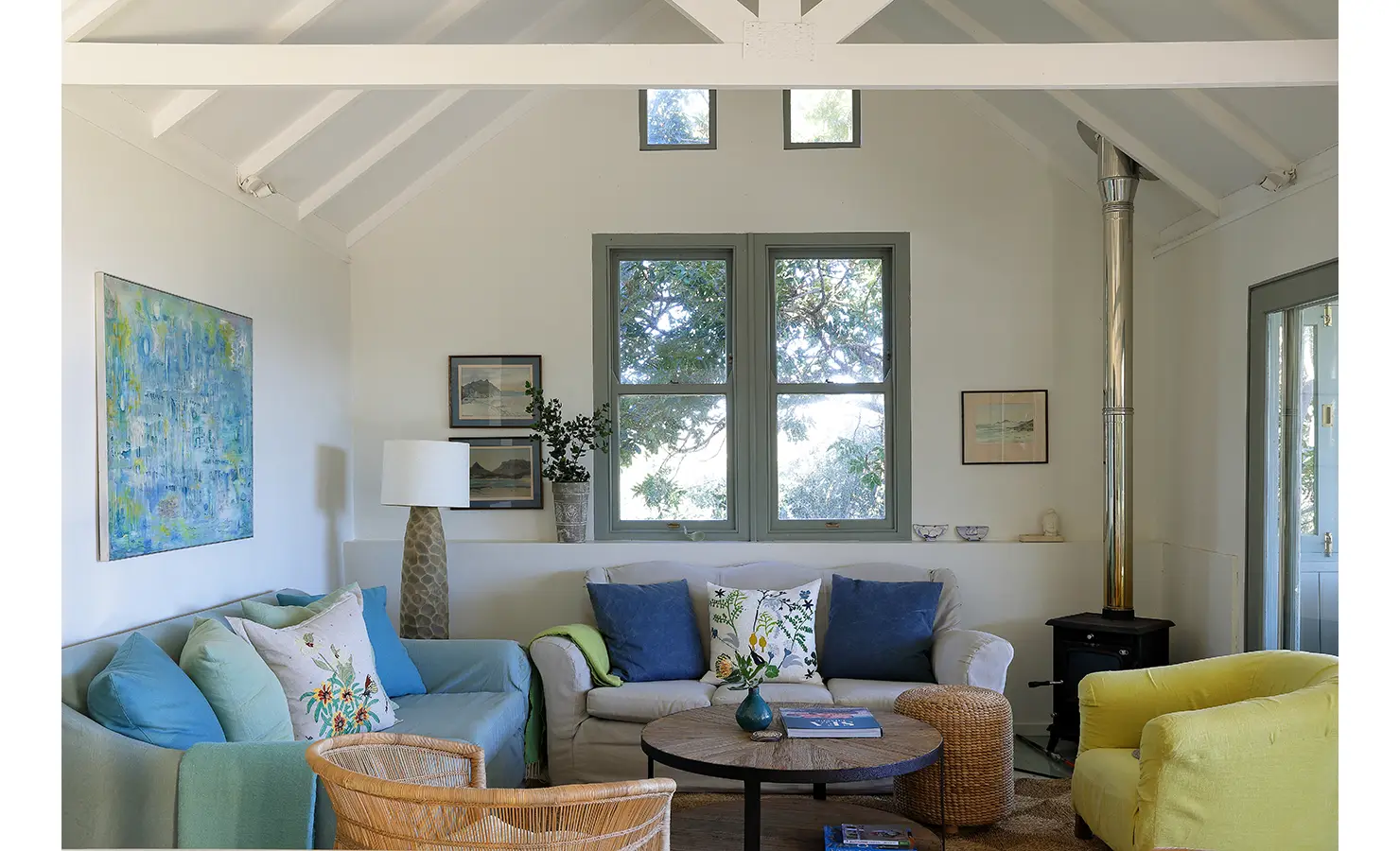 Perfect Hideaways: Light-filled sitting room with vaulted ceiling, layered sofas and wicker textures around a round coffee table, wood-burning stove and art for cosy charm, Amongst The Trees, Scarborough.