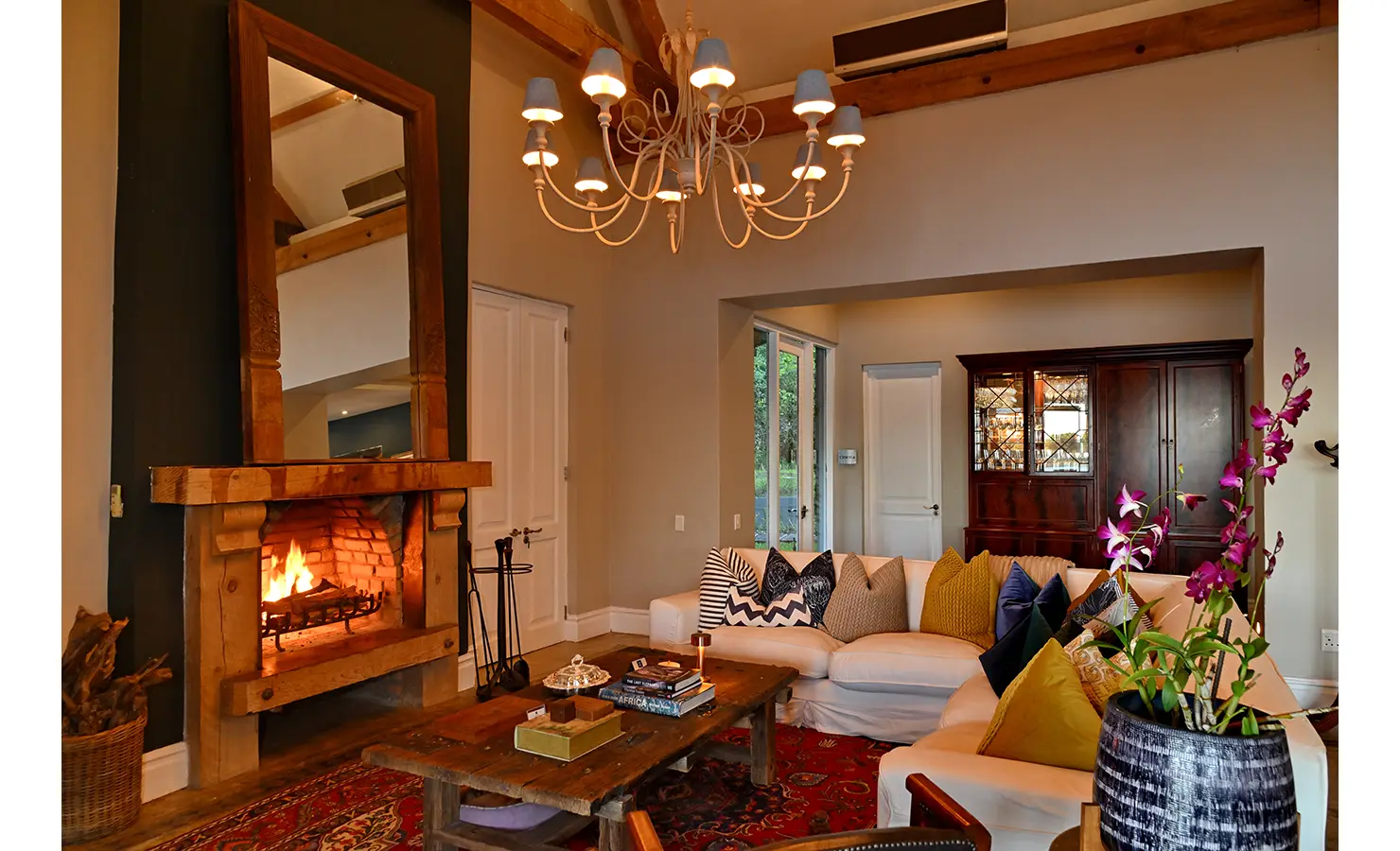 Perfect Hideaways: Cosy lounge with a roaring fireplace, wooden mantel, and colourful scatter cushions creating a warm and inviting atmosphere, Tanyati Villa, Livingstone