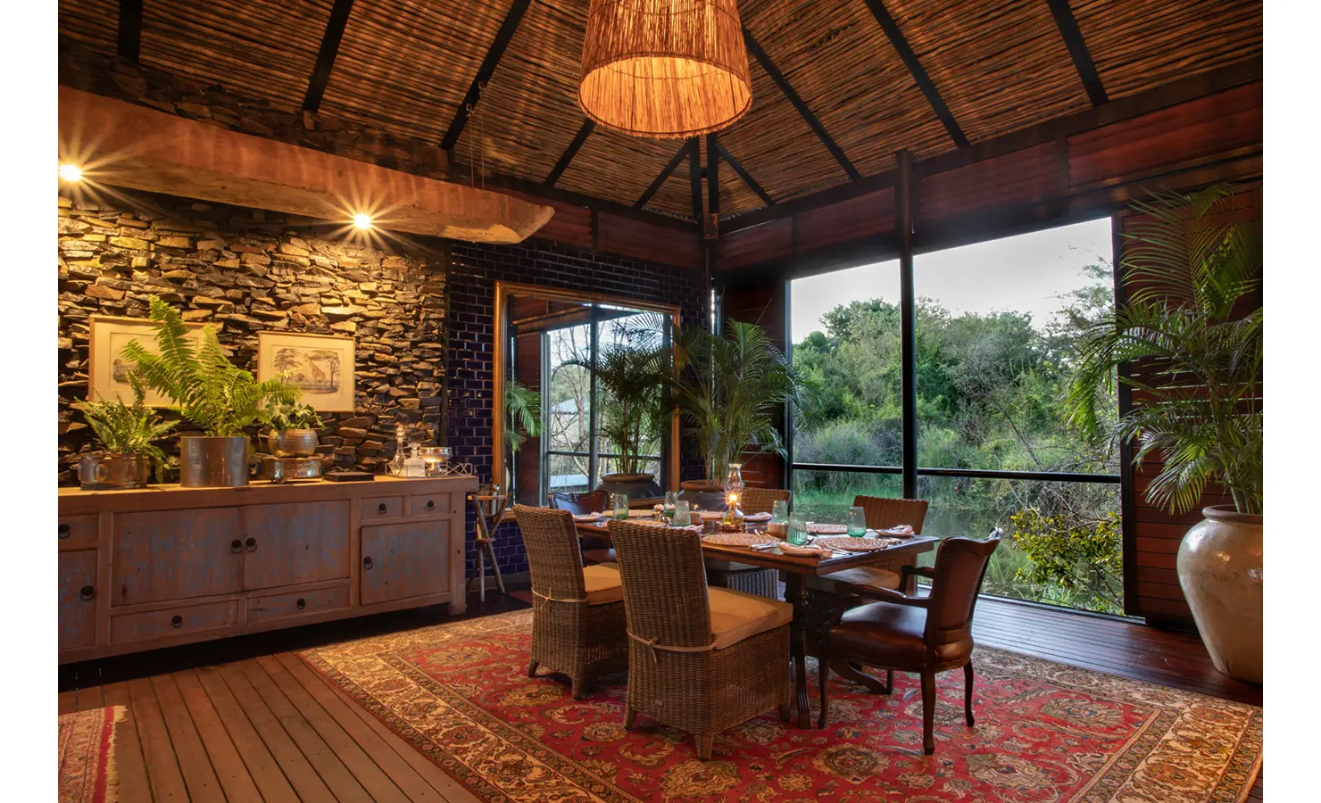 Perfect Hideaways: intimate dining area with wicker chairs around a wooden table, stacked-stone and deep blue tile walls, opening to green riverine views — Mukwa River Lodge, Livingstone