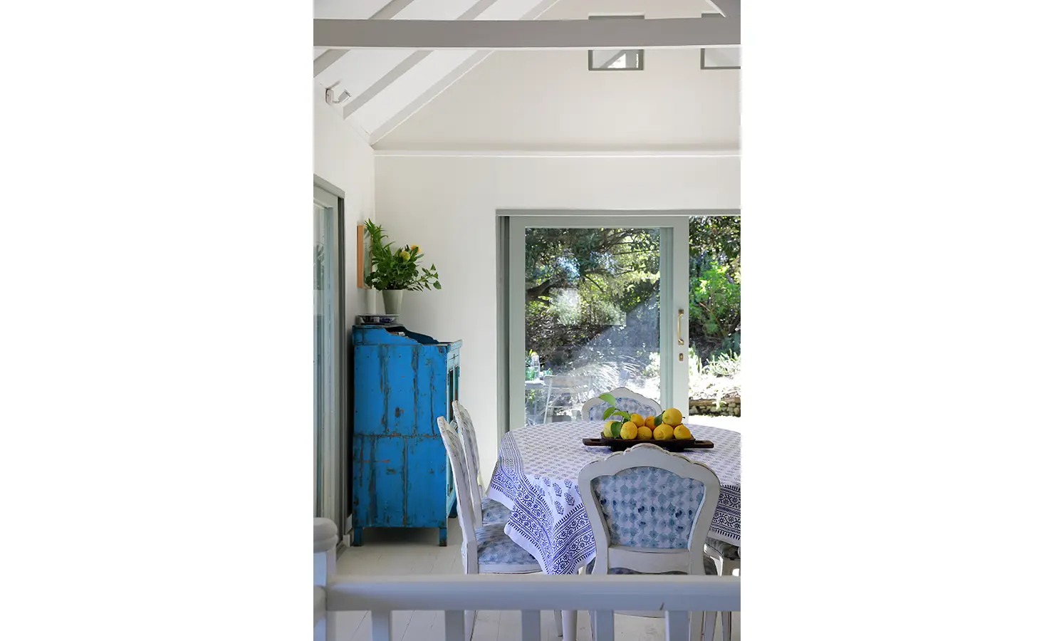 Perfect Hideaways: Sunny breakfast nook with a weathered blue cupboard, botanical greenery and lemons on a patterned cloth beside garden-facing sliders, Amongst The Trees, Scarborough.