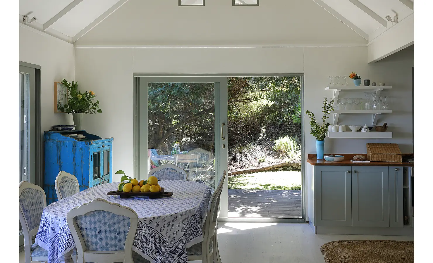 Perfect Hideaways: Dining table beside open shelving and sage cabinetry, sliding doors to a leafy garden and timber countertops adding warmth, Amongst The Trees, Scarborough.