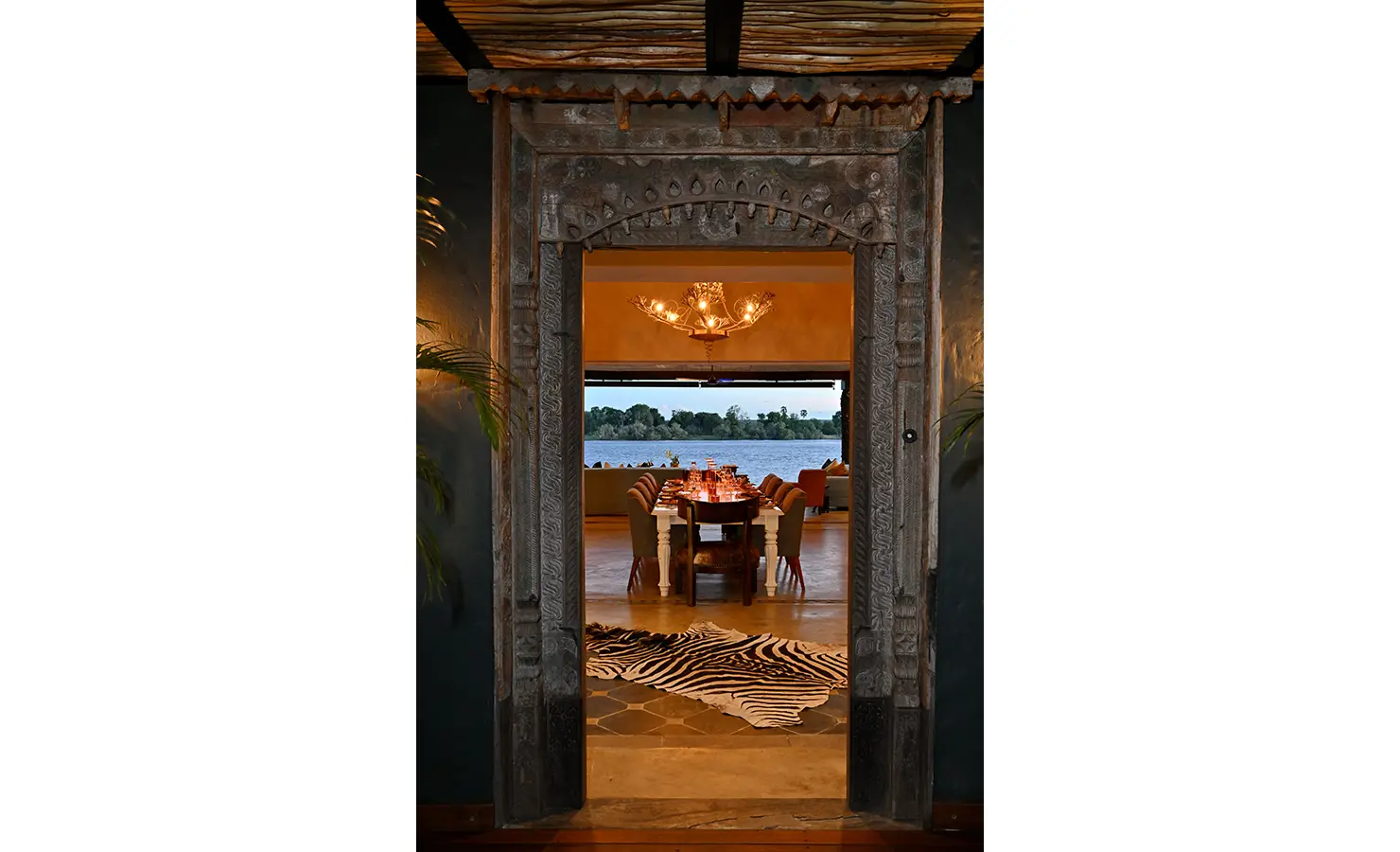 Perfect Hideaways: Ornate carved doorway framing a view of the dining area and river beyond, accented with a zebra hide rug, Tanyati Villa, Livingstone