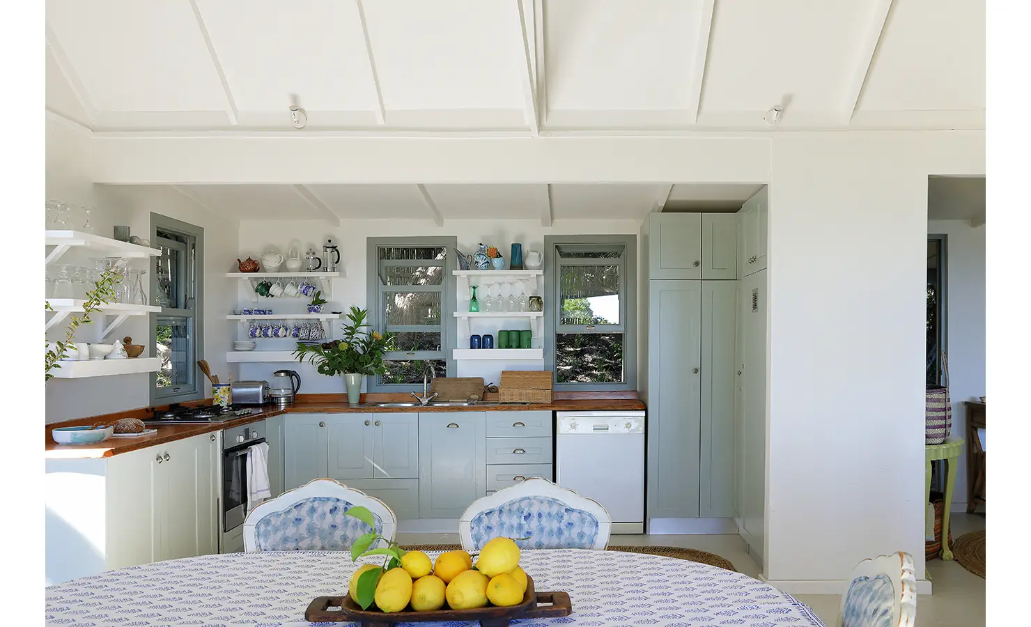 Perfect Hideaways: Cottage kitchen with open shelves, sage units and wooden worktops, viewed from the dining table laid with a blue print and fresh lemons, Amongst The Trees, Scarborough.