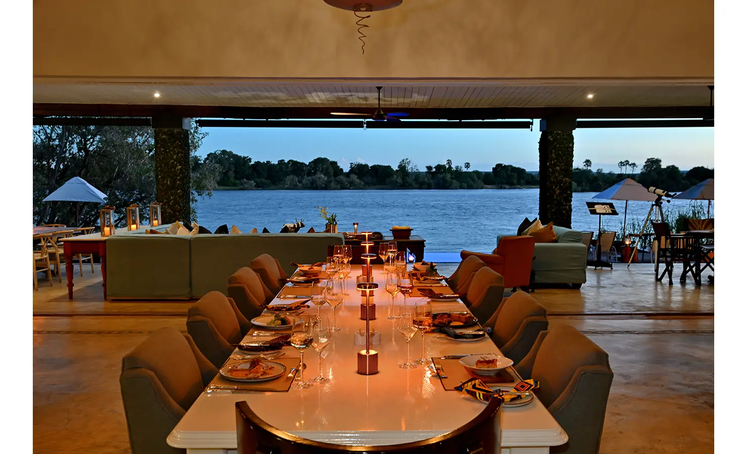 Perfect Hideaways: Evening dining setup with a long candlelit table under a covered terrace, offering uninterrupted river views, Tanyati Villa, Livingstone