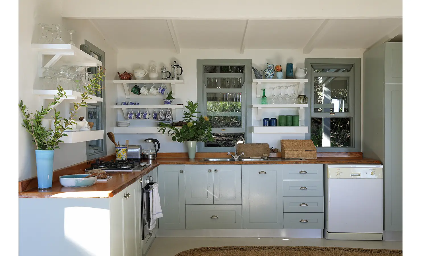Perfect Hideaways: Kitchen detail with gas hob, open shelves of blue-and-white crockery and a vase of foliage — homely and practical, Amongst The Trees, Scarborough.