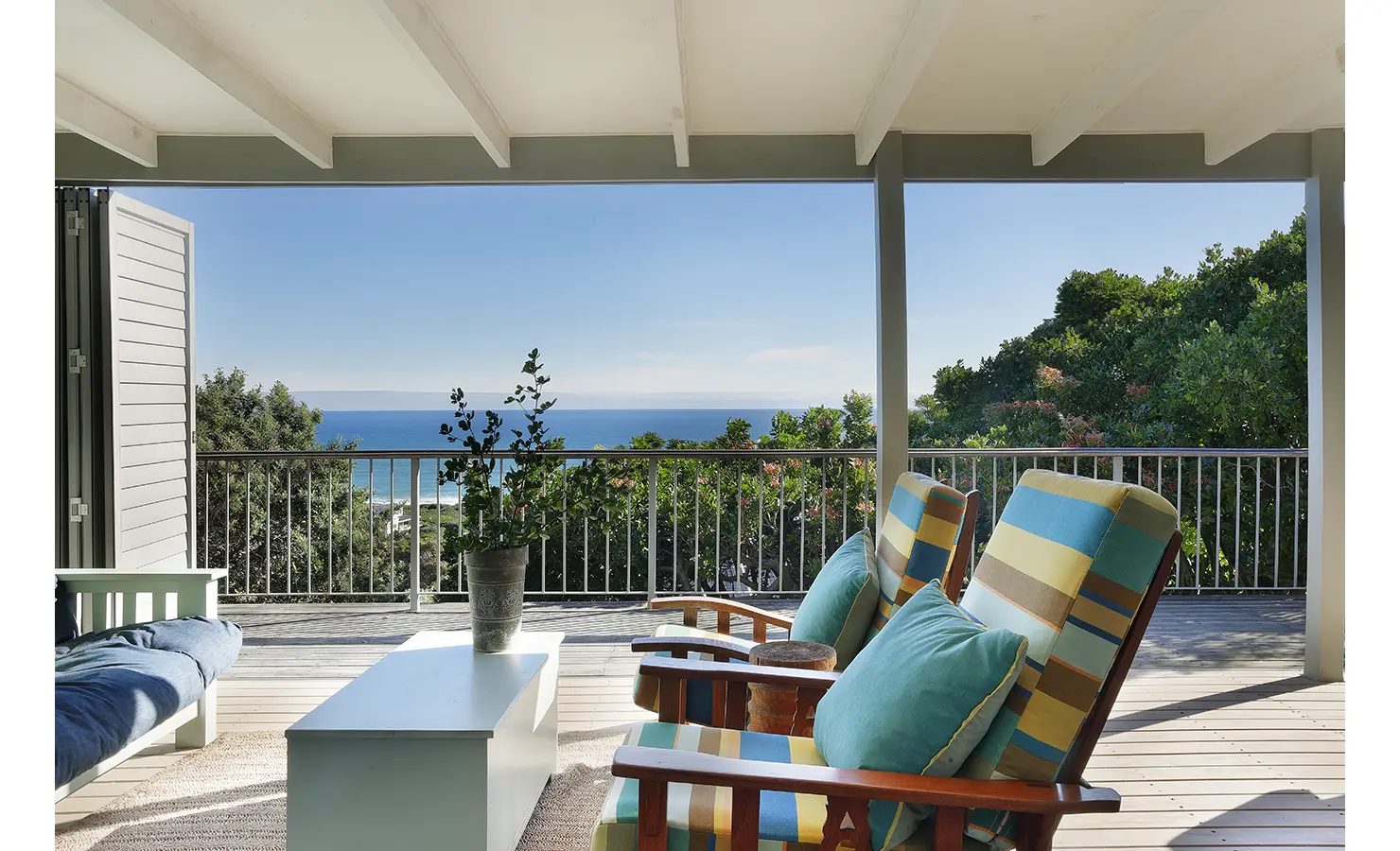 Perfect Hideaways: Covered deck seating with striped cushioned armchairs and sea-blue pillows overlooking the water, potted greenery and a simple coffee bench — serene outlook, Amongst The Trees, Scarborough.