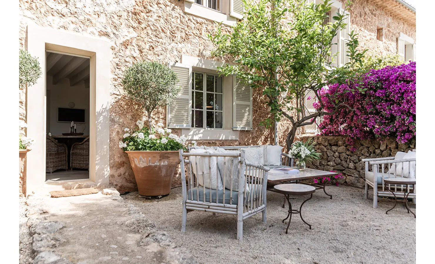 Perfect Hideaways: A tranquil courtyard retreat with vintage whitewashed furniture, terracotta pots brimming with geraniums, and vibrant fuchsia bougainvillea climbing the rustic stone walls. Finca Es Rafal, Alaró