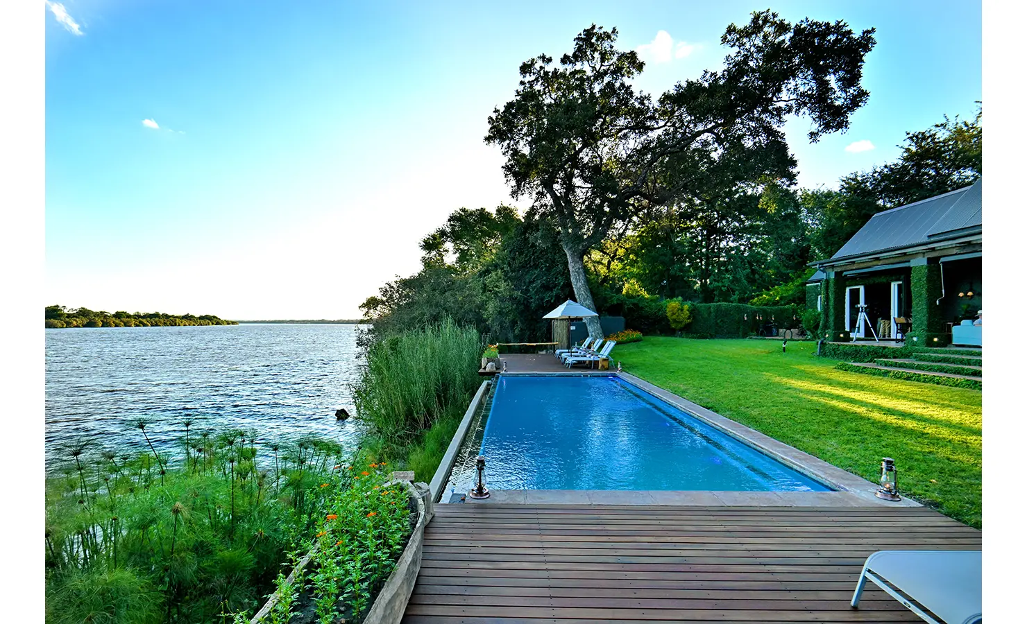 Perfect Hideaways: Riverside lap pool surrounded by a timber deck, sun loungers, and vibrant gardens, Tanyati Villa, Livingstone