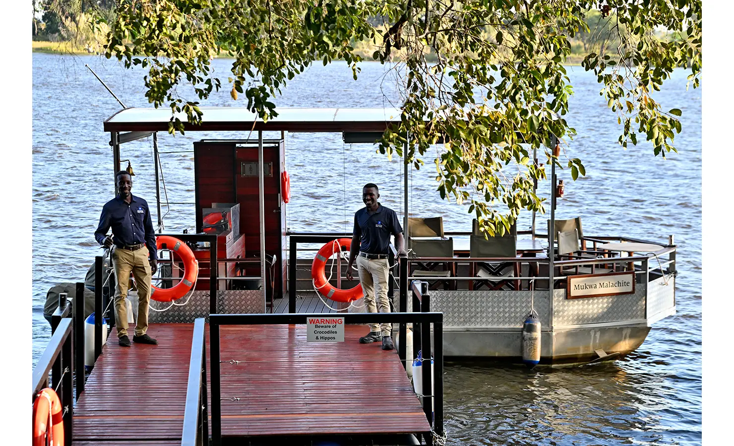 Perfect Hideaways: Two smiling hosts welcoming guests aboard a riverboat named Mukwa Malachite, docked on the calm Zambezi River, Tanyati Villa, Livingstone