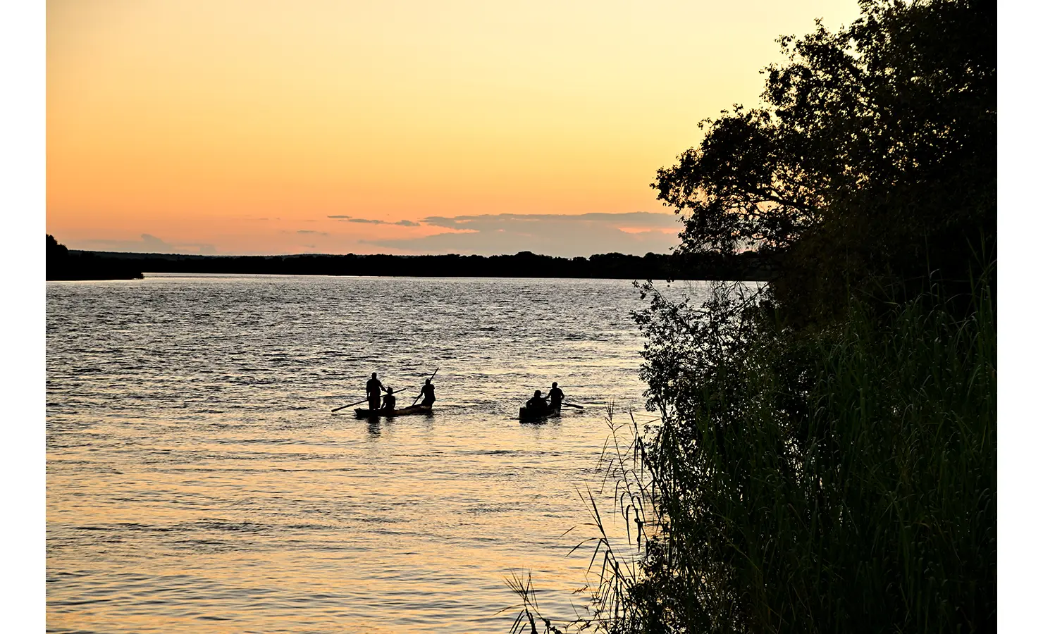 Perfect Hideaways: Silhouetted figures paddling traditional canoes at sunset against the glowing orange sky, Tanyati Villa, Livingstone