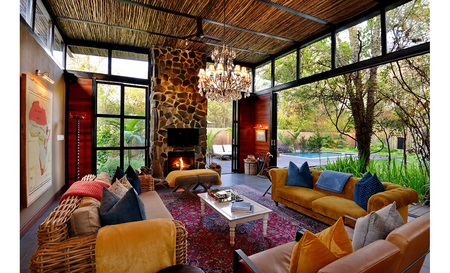 Perfect Hideaways: double-volume lounge with stone fireplace, crystal chandelier, rattan and velvet sofas and wide doors to the pool garden — Mukwa River Lodge, Livingstone