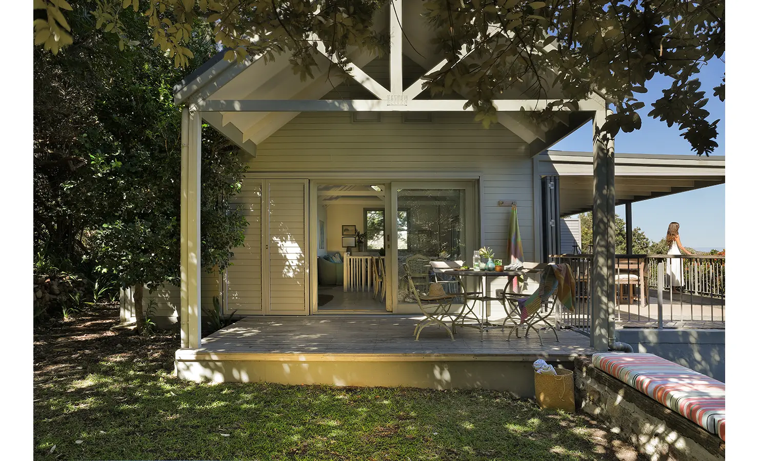 Perfect Hideaways: Garden-facing deck beneath exposed trusses with café table and wraparound verandah, ocean glimpses through the trees, Amongst The Trees, Scarborough.