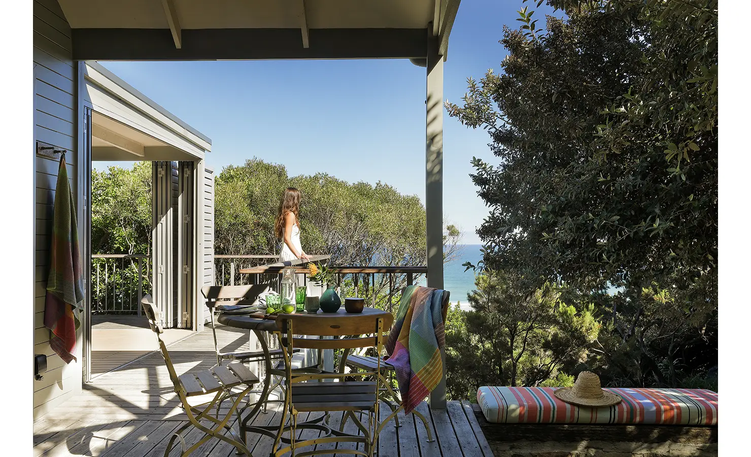 Perfect Hideaways: Breakfast table on the deck with ceramics and a colourful throw, guest leaning on the rail to drink in the sea view — slow coastal mornings, Amongst The Trees, Scarborough.