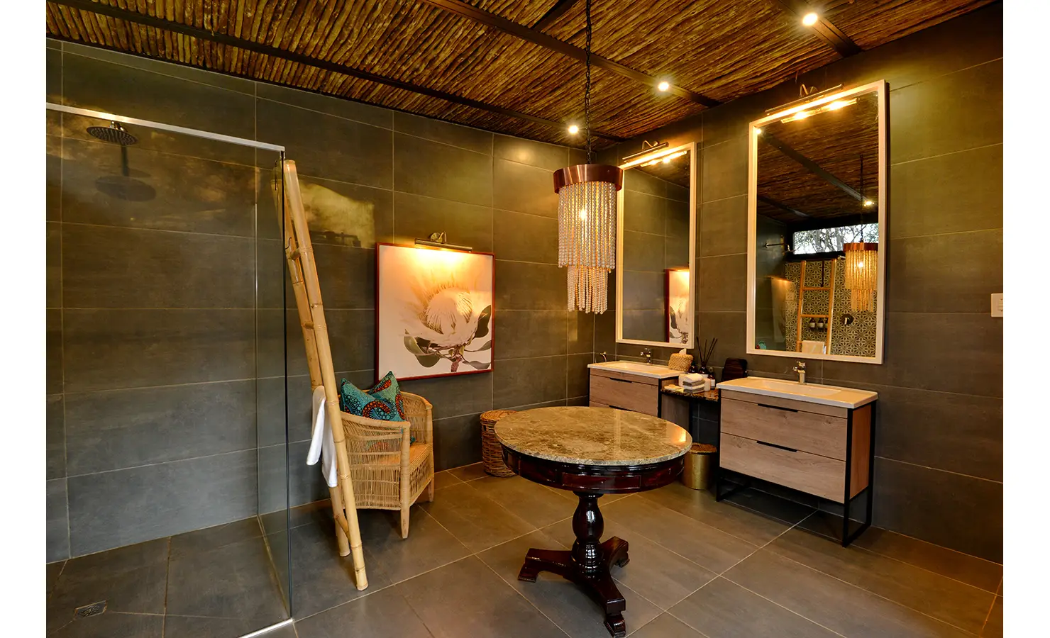 Perfect Hideaways: spacious bathroom with walk-in shower, twin vanities, beaded chandelier, bamboo ladder and framed protea artwork — Mukwa River Lodge, Livingstone