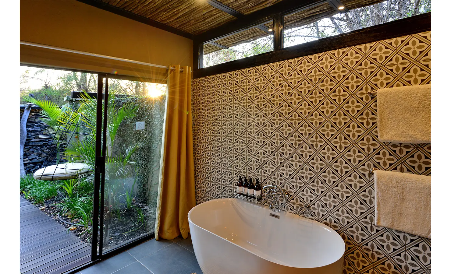 Perfect Hideaways: patterned-tile bathroom with a freestanding tub beside sliding doors to a private garden, morning sun filtering in — Mukwa River Lodge, Livingstone