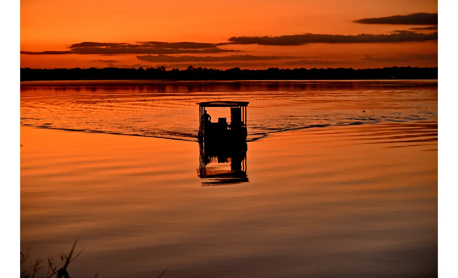 Perfect Hideaways: Silhouette of a boat gliding across the Zambezi River at sunset, with the water glowing in deep orange tones, Tanyati Villa, Livingstone