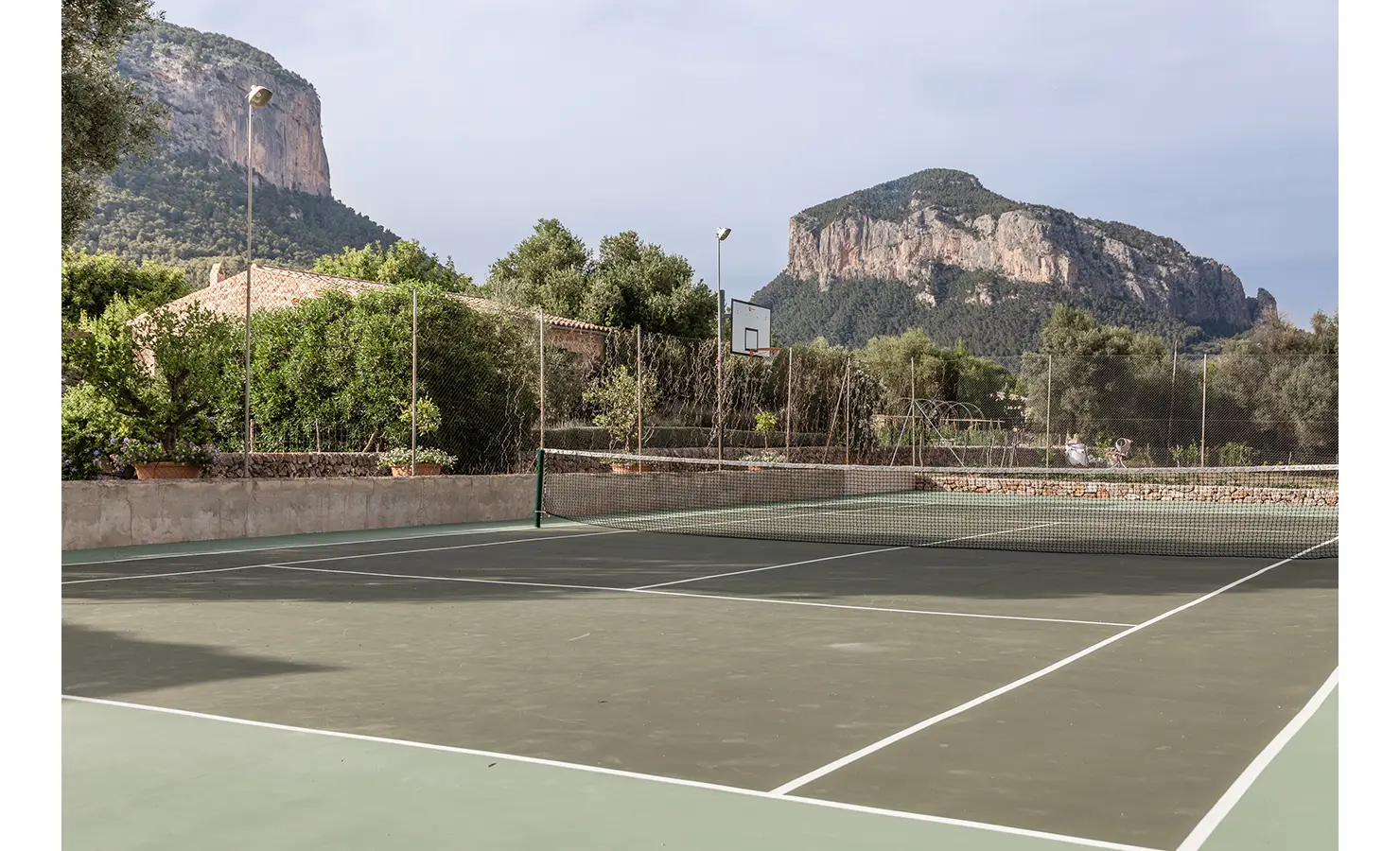 Perfect Hideaways: A full-size tennis court nestled among olive trees and framed by the dramatic cliffs of Alaró, offering a spectacular sporting backdrop under open skies. Finca Es Rafal, Alaró