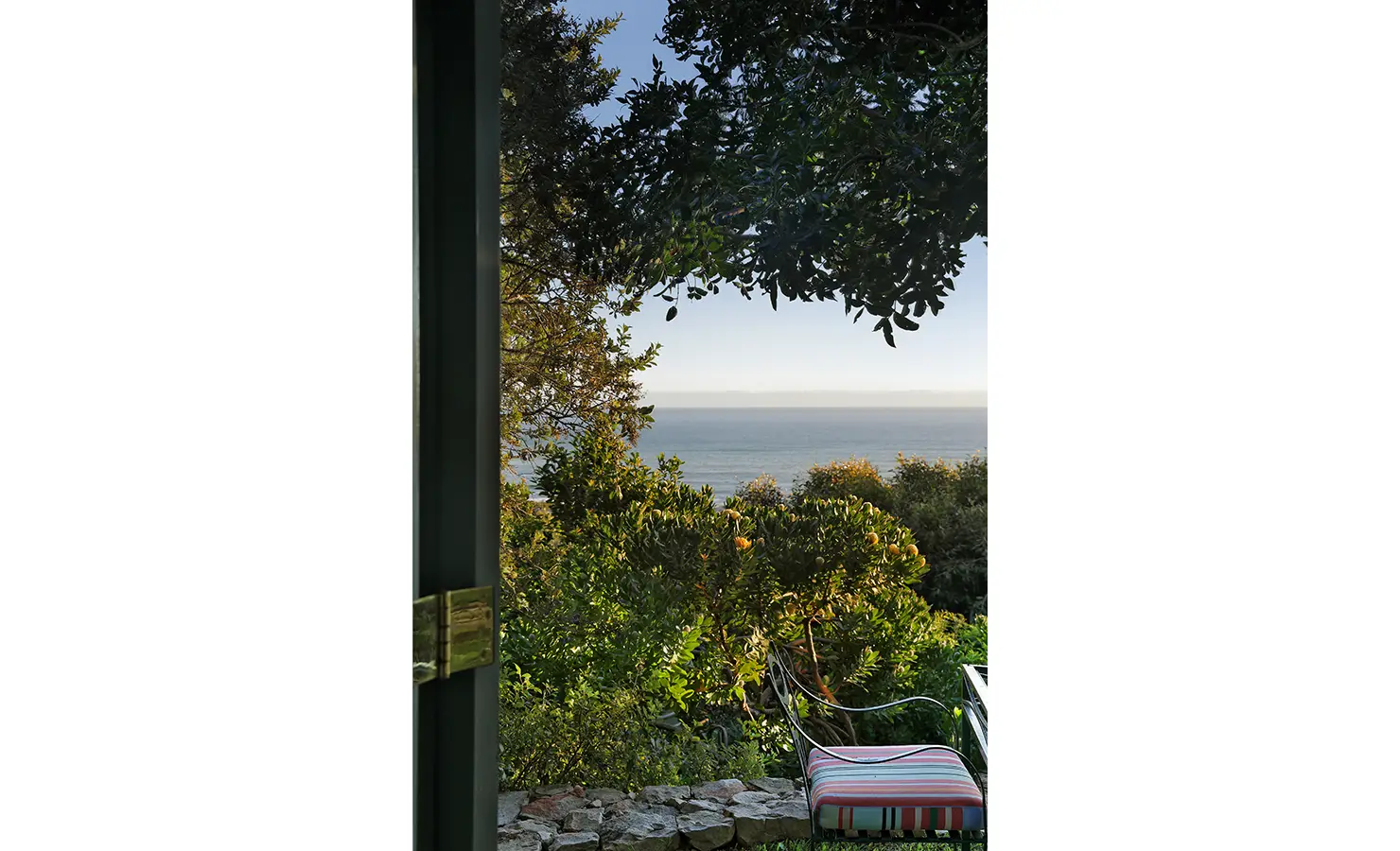 Perfect Hideaways: View from the doorway to stone edging and a striped bench cushion, lush foliage and the ocean beyond — leafy lookout, Amongst The Trees, Scarborough.