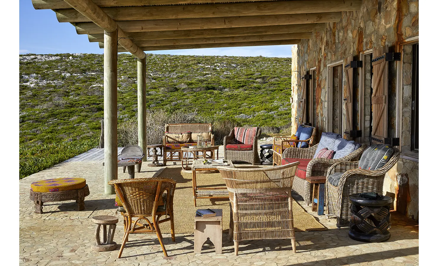 Perfect Hideaways: A shaded veranda furnished with eclectic woven chairs and rustic wooden tables opens out to indigenous fynbos-covered hills. Fynbos Fort, Plettenberg Bay.