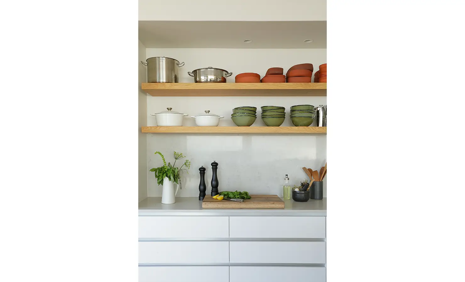 Perfect Hideaways: A detail of open shelving in the kitchen showcasing green bowls, terracotta dishes, and stainless-steel cookware, with herbs and utensils thoughtfully arranged on a pristine counter. Whales Breath, De Kelders.
