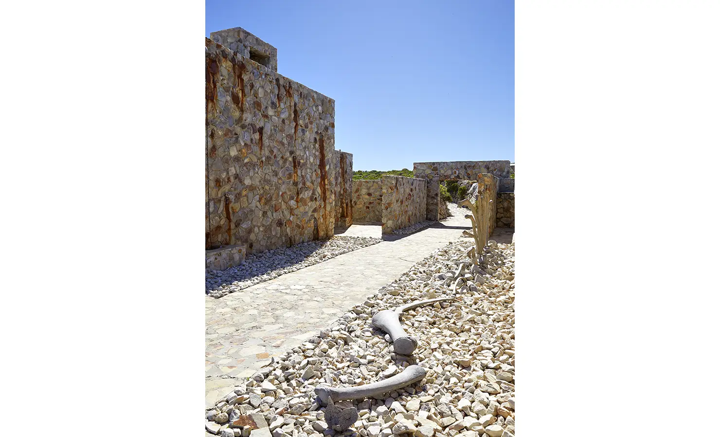 Perfect Hideaways: A sculptural display of large bones weaves through a bed of white stone pebbles, nestled among rugged stone walls and pathways. Fynbos Fort, Plettenberg Bay.