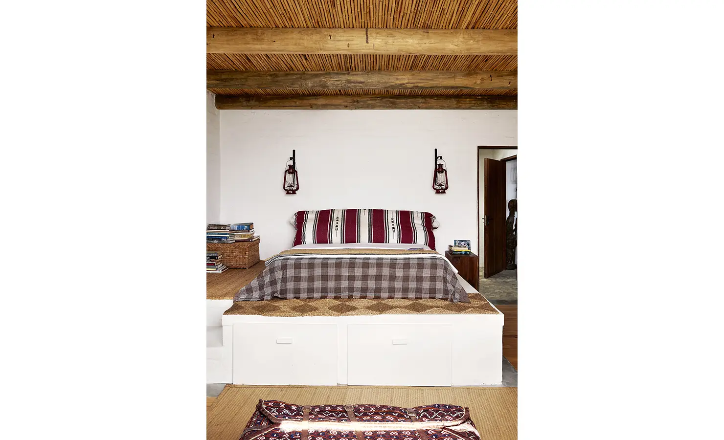 Perfect Hideaways: A raised bed with layered textiles and woven baskets sits beneath a reed ceiling, creating a rustic and inviting bedroom space. Fynbos Fort, Plettenberg Bay.