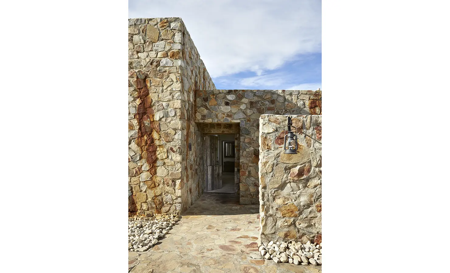 Perfect Hideaways: The entrance to the hideaway is framed by warm-toned stone walls and an old lantern, inviting guests into its earthy, fort-like design. Fynbos Fort, Plettenberg Bay.