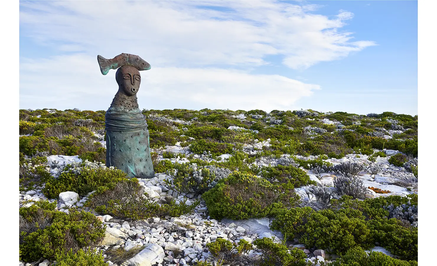Perfect Hideaways: A bronze statue of a serene figure with a fish on its head stands among coastal scrub, adding a mystical touch to the wild fynbos landscape. Fynbos Fort, Plettenberg Bay.