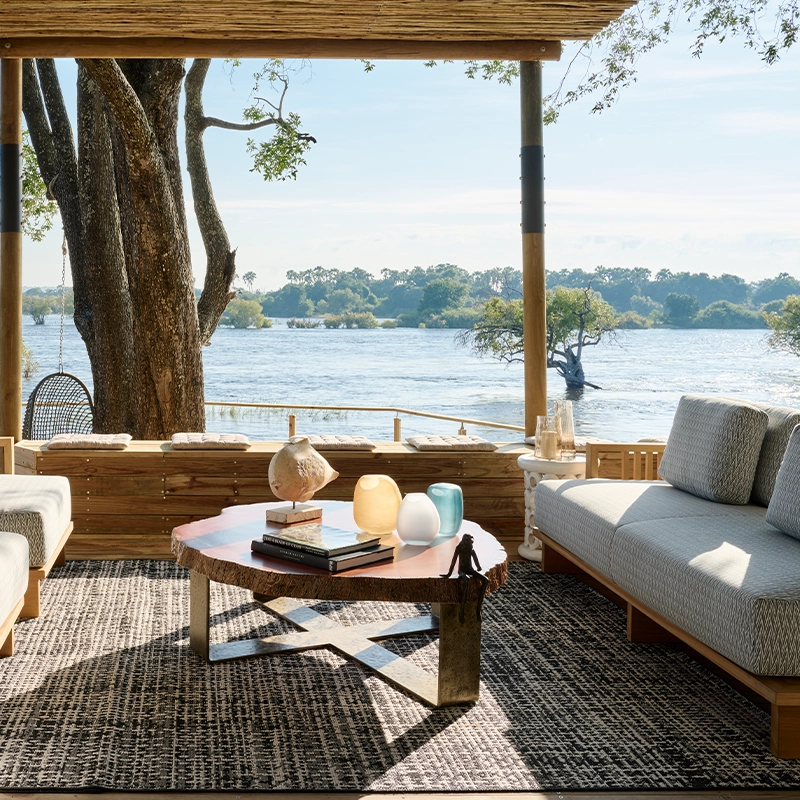 Perfect Hideaways: Open-air riverfront lounge beneath a timber pergola, with cushioned sofas, woven rug and a live-edge coffee table overlooking the Zambezi, Rapid's View Villa, Zambezi National Park