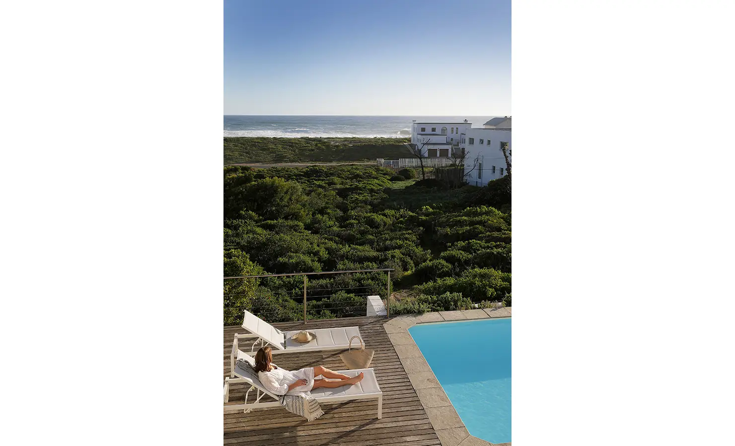 Perfect Hideaways: poolside deck with a guest reclining on a white sun lounger, glass balustrade, coastal fynbos and ocean horizon beyond under a clear blue sky, Blanc de Blanc, Yzerfontein