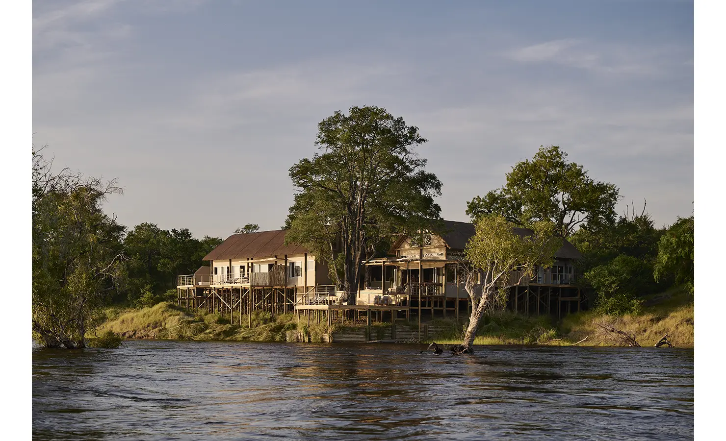 Perfect Hideaways: Riverbank safari villa on timber stilts with wraparound decks and towering trees seen from the Zambezi, Rapid's View Villa, Zambezi National Park