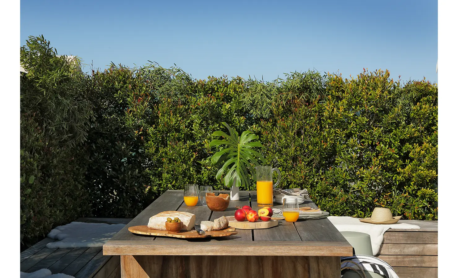 Perfect Hideaways: rustic outdoor table laid for breakfast with fresh bread, fruit and orange juice, shaded by lush hedging and a bright blue sky, Blanc de Blanc, Yzerfontein