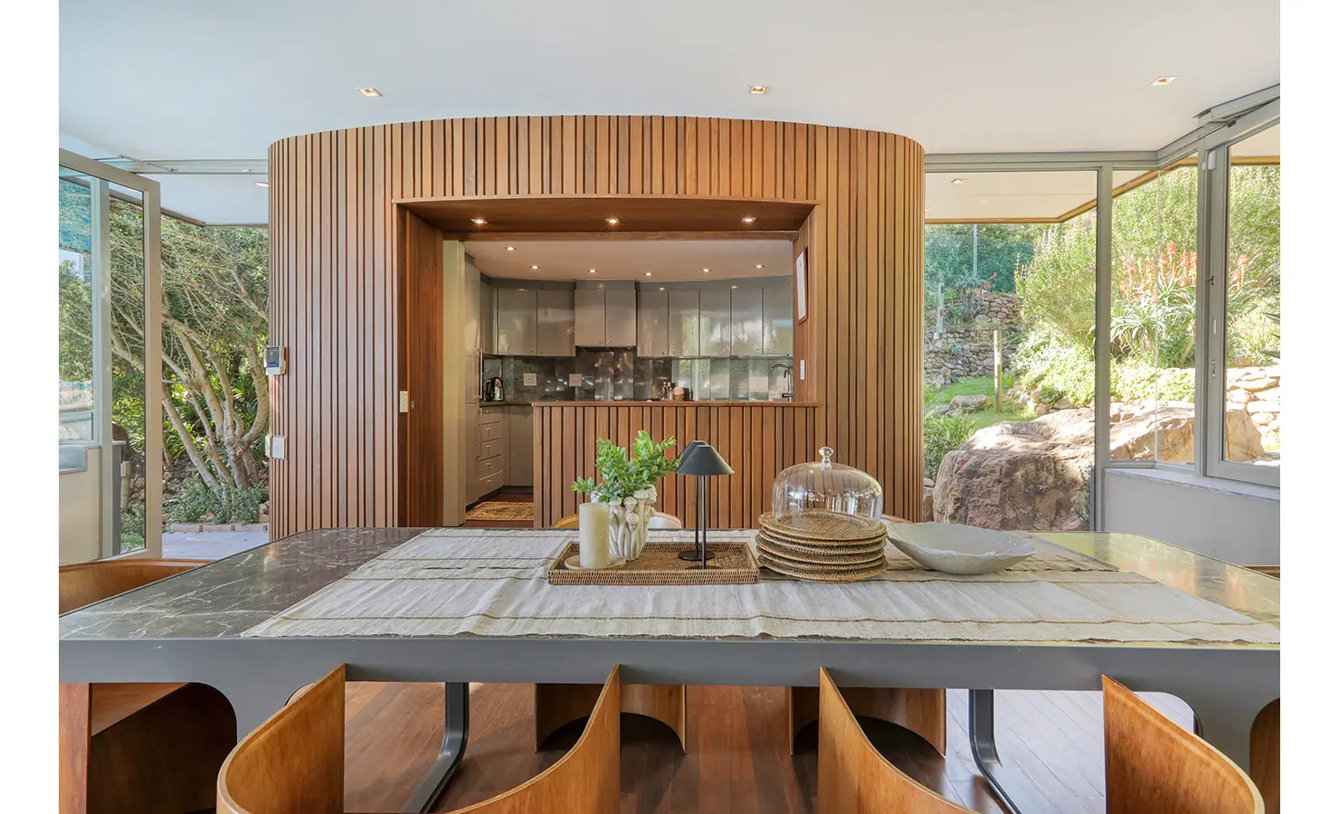 Perfect Hideaways: Dining room facing a curved slatted timber kitchen pod with garden views through floor‑to‑ceiling glass, Spa House, Hout Bay