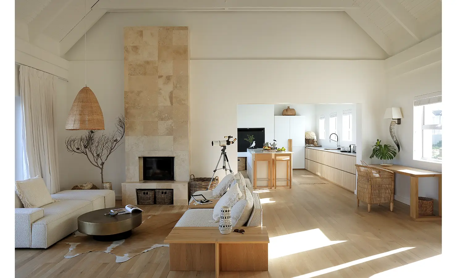 Perfect Hideaways: airy open-plan living room with stone-clad fireplace, cream bouclé sofas and telescope, leading to a light-wood kitchen with island, Blanc de Blanc, Yzerfontein