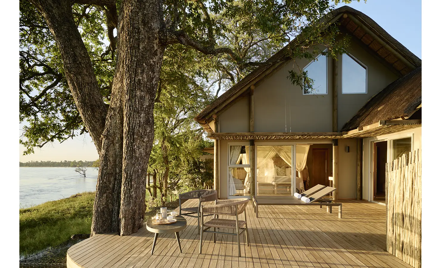 Perfect Hideaways: Thatched, tented suite with mosquito-netted bed opening onto a broad timber deck with loungers beneath ancient trees beside the river. Hippo Creek Villa, Zambezi National Park.