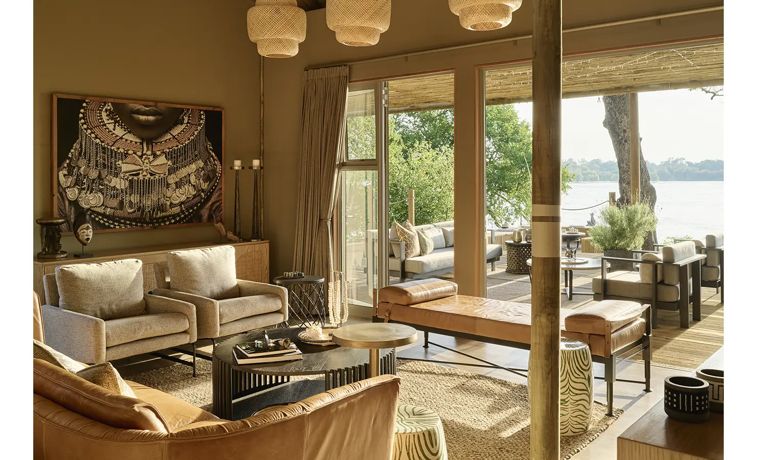 Perfect Hideaways: Warm, textural living room with woven pendants and curated African art, sliding doors leading to the riverfront deck. Hippo Creek Villa, Zambezi National Park.