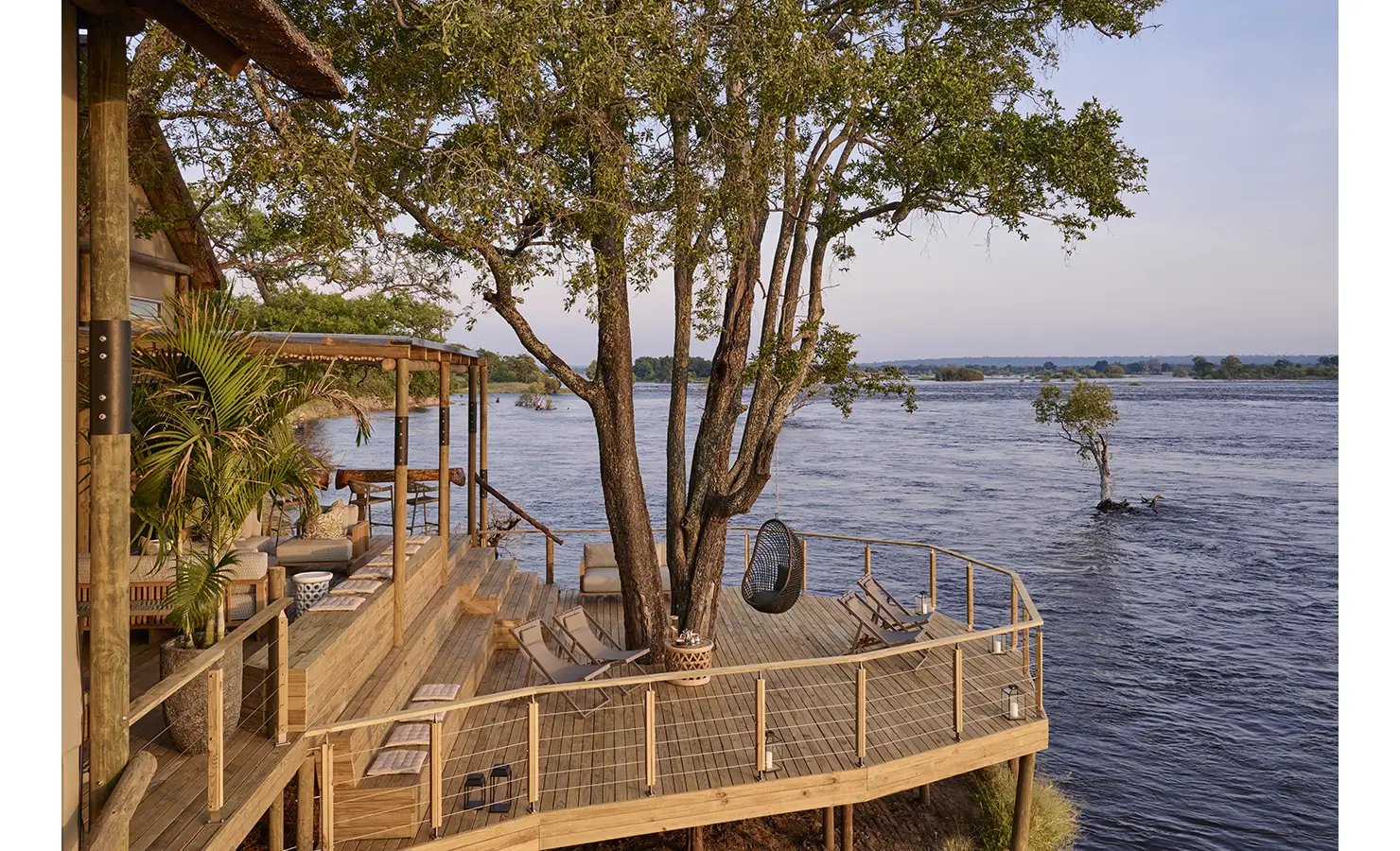 Perfect Hideaways: Expansive tiered timber deck wrapped around a mature tree with loungers and a hanging chair over the river, Rapid's View Villa, Zambezi National Park