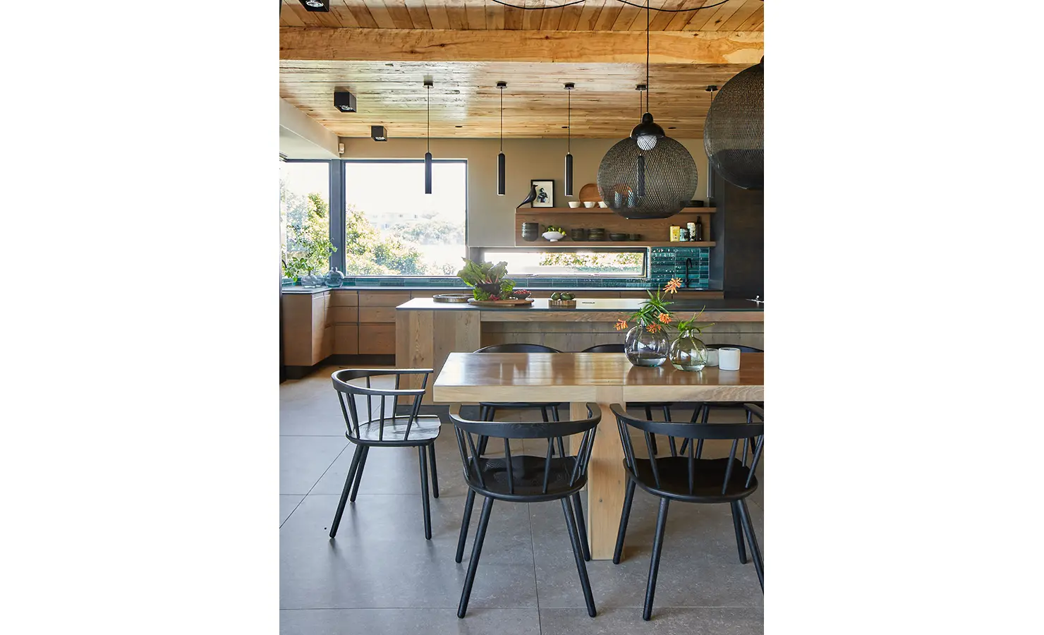 Perfect Hideaways: A view across the kitchen reveals a wood-ceilinged space with stylish pendant lights, an island filled with fresh produce, and a large timber dining table. St Austel, Kenton-on-Sea