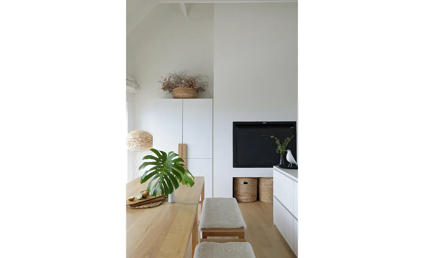 Perfect Hideaways: detail of dining nook with wooden table, monstera leaf in a vase and woven baskets beside sleek white cabinetry, Blanc de Blanc, Yzerfontein