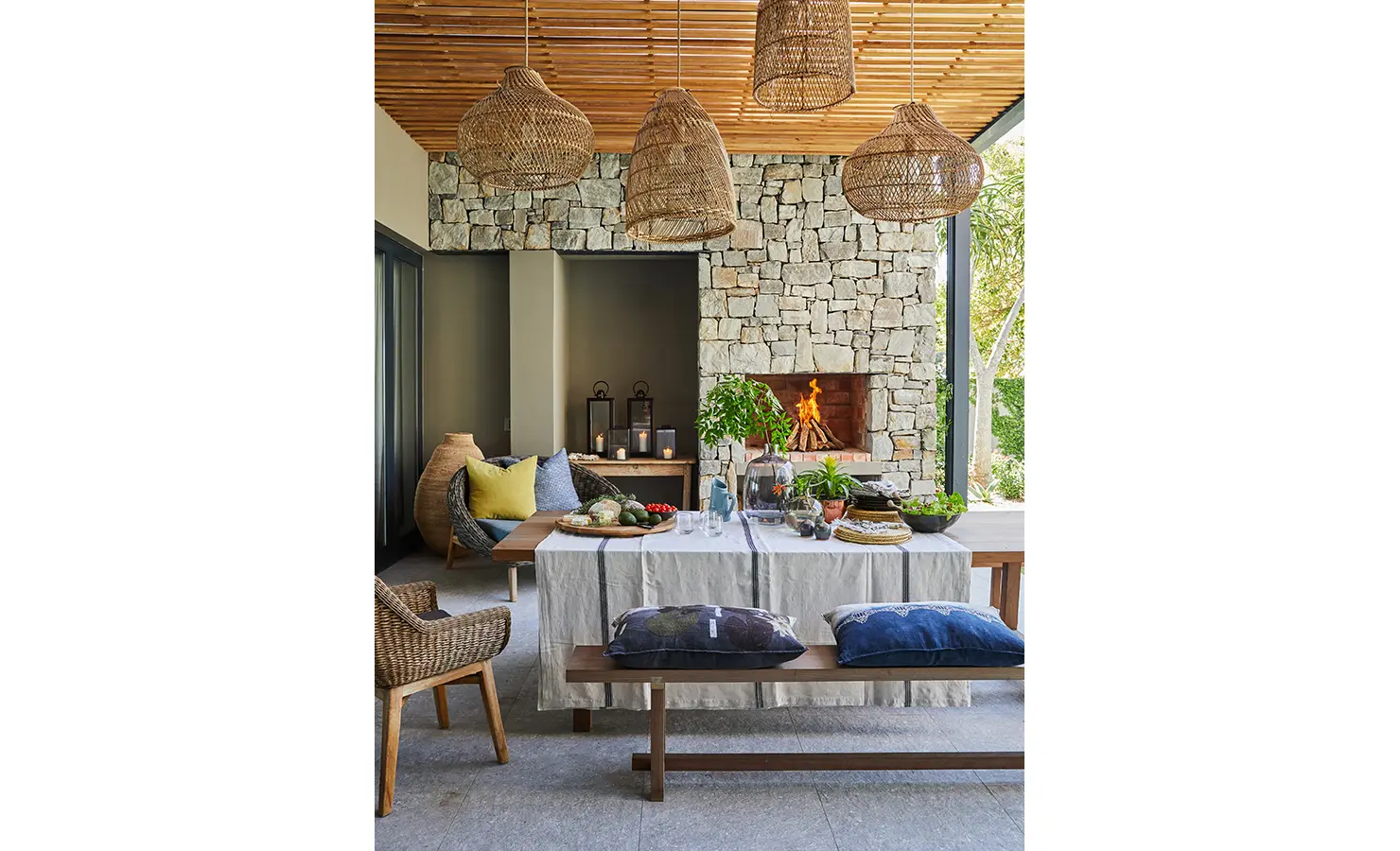Perfect Hideaways: A charming indoor braai area with wicker pendant lights, stone fireplace, and a rustic table laid with fresh ingredients and colourful tableware. St Austel, Kenton-on-Sea