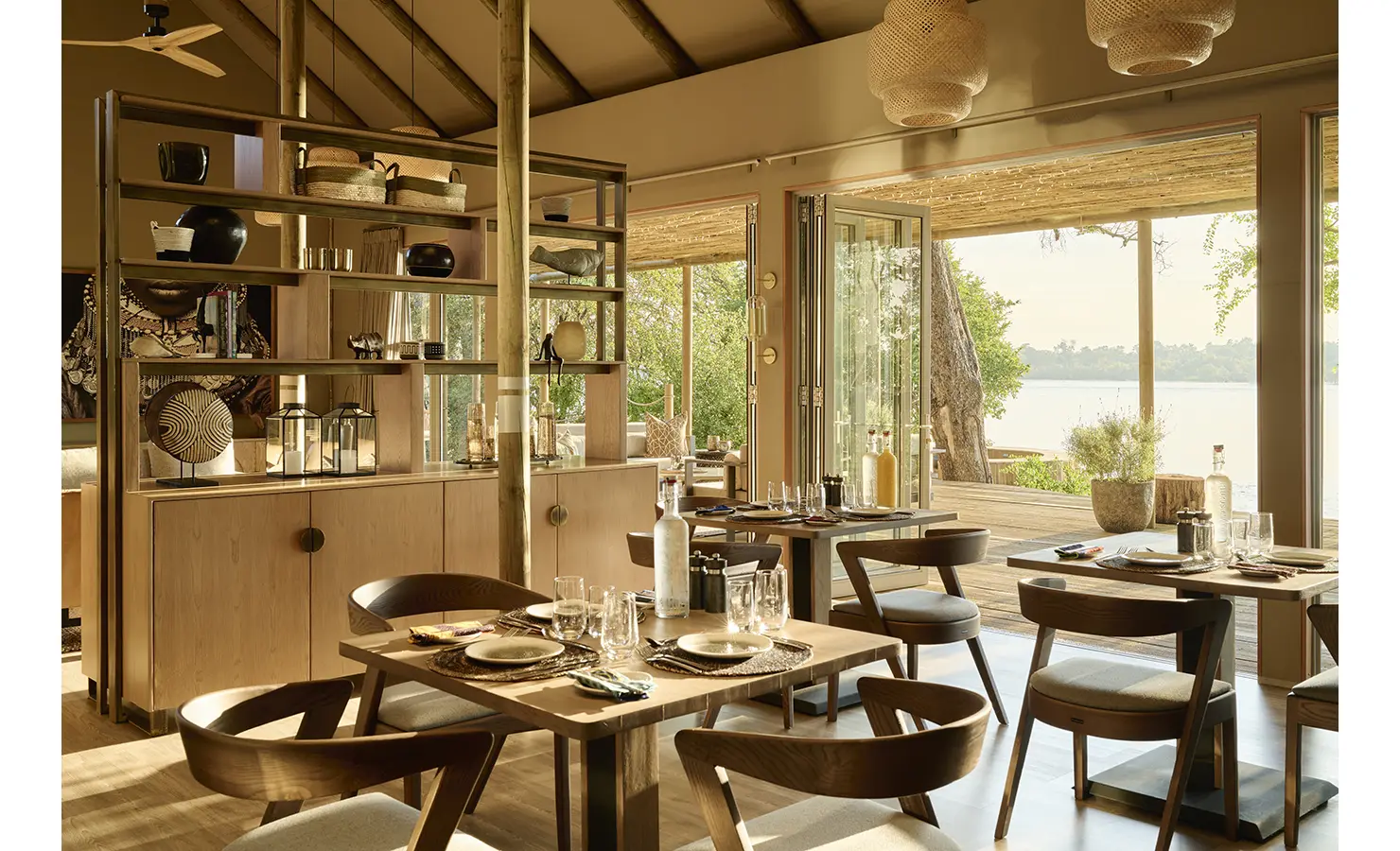 Perfect Hideaways: Intimate dining room with contemporary timber tables and open shelving, folding doors to the river-facing terrace. Hippo Creek Villa, Zambezi National Park.