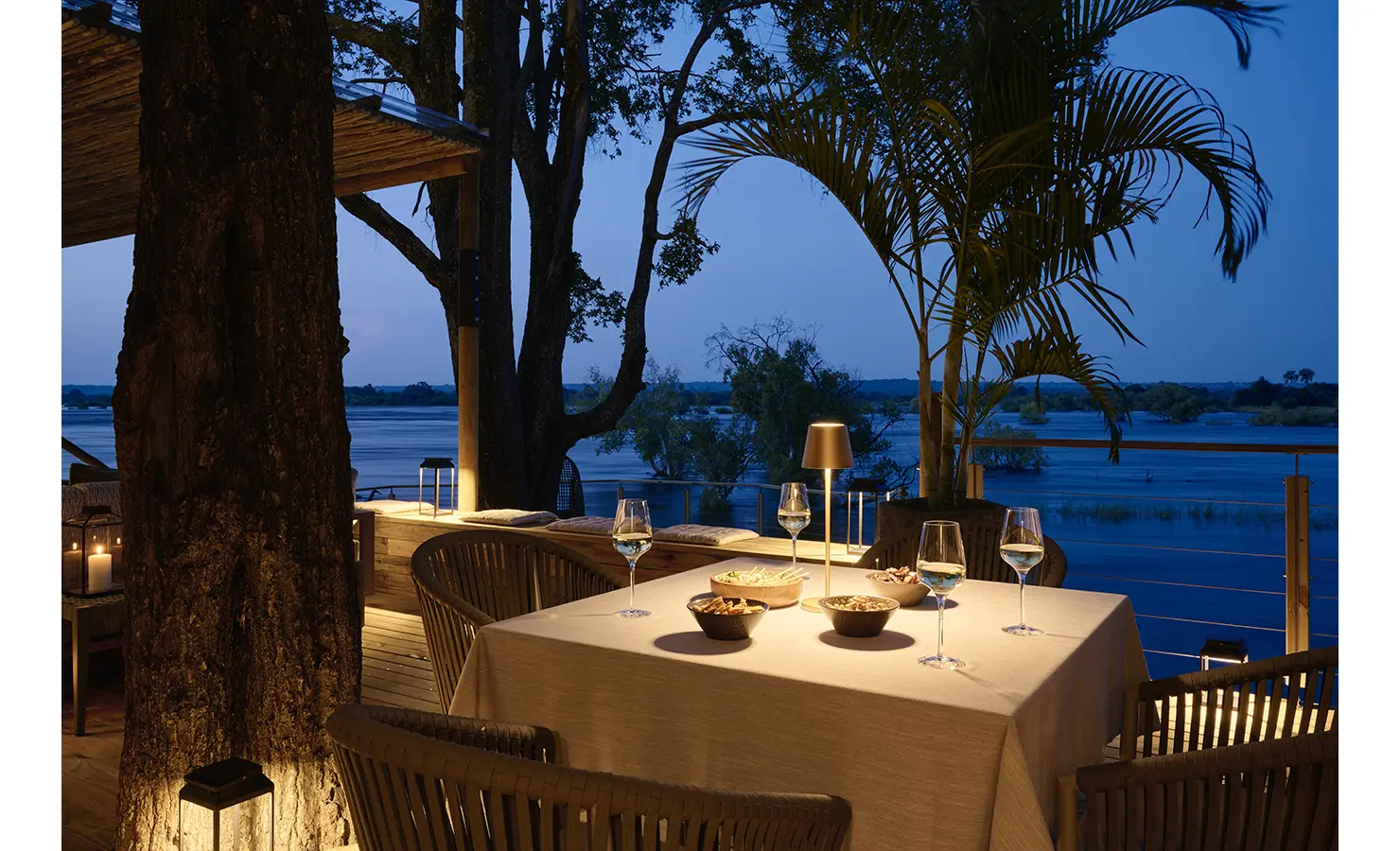 Perfect Hideaways: Intimate candlelit dining table on the deck amid trees and palms with dusk river views, Rapid's View Villa, Zambezi National Park
