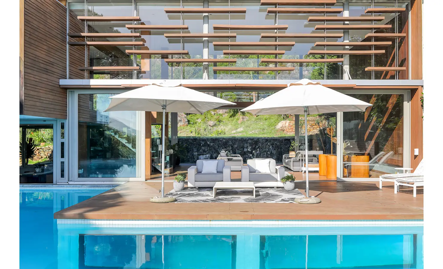 Perfect Hideaways: Poolside view of the glass‑and‑timber façade with adjustable horizontal louvres and a shaded outdoor lounge, Spa House, Hout Bay